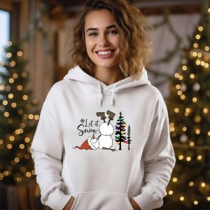 May include: White hoodie with a black and white snowman design. The snowman is wearing a Santa hat and has a brown stick for arms. The text 'Let it Snow' is written above the snowman. There is a small Christmas tree with colorful lights behind the snowman.